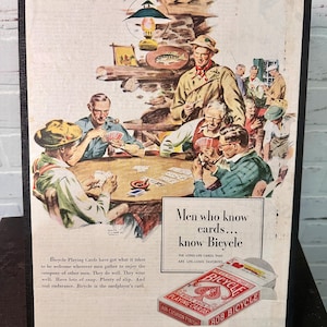 Może przedstawiać: Reklama w stylu vintage dla kart do gry Bicycle. Obraz przedstawia grupę mężczyzn grających w karty. Tekst brzmi: &bdquo;Mężczyźni, kt&oacute;rzy znają karty... znają Bicycle&rdquo;. Reklama pochodzi z The Saturday Evening Post.