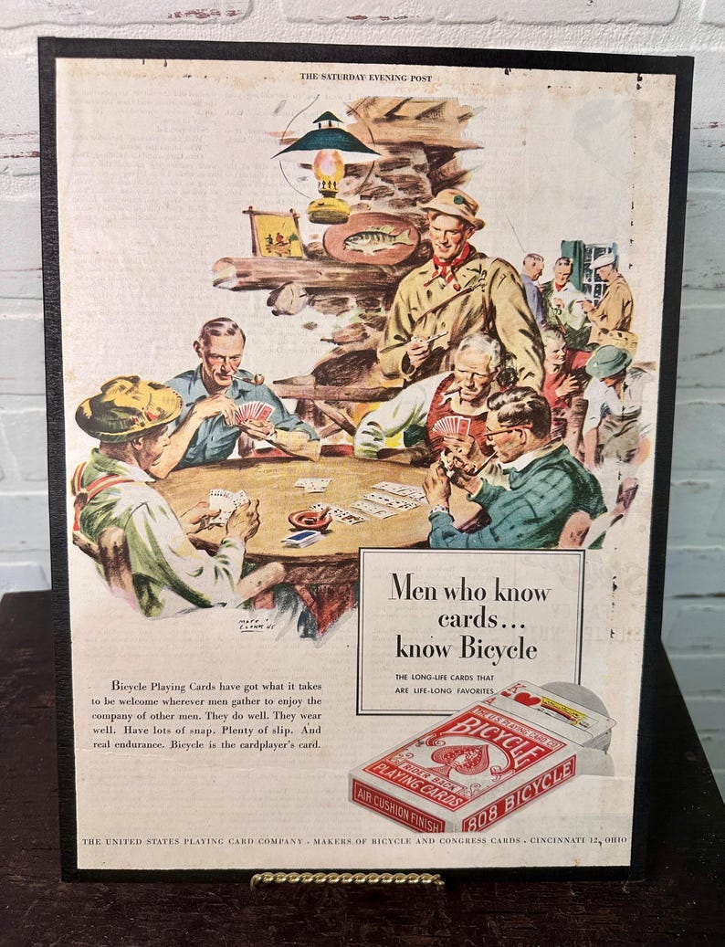 Może przedstawiać: Reklama w stylu vintage dla kart do gry Bicycle. Obraz przedstawia grupę mężczyzn grających w karty. Tekst brzmi: &bdquo;Mężczyźni, kt&oacute;rzy znają karty... znają Bicycle&rdquo;. Reklama pochodzi z The Saturday Evening Post.