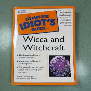 May include: A paperback book titled The Complete Idiot's Guide to Wicca and Witchcraft by Denise Zimmermann and Katherine A. Gleason. The cover features an orange border, blue text, and a circular purple graphic depicting a pentagram symbol.