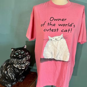 May include: Pink t-shirt with a white cat illustration and the text "Owner of the world's cutest cat!"