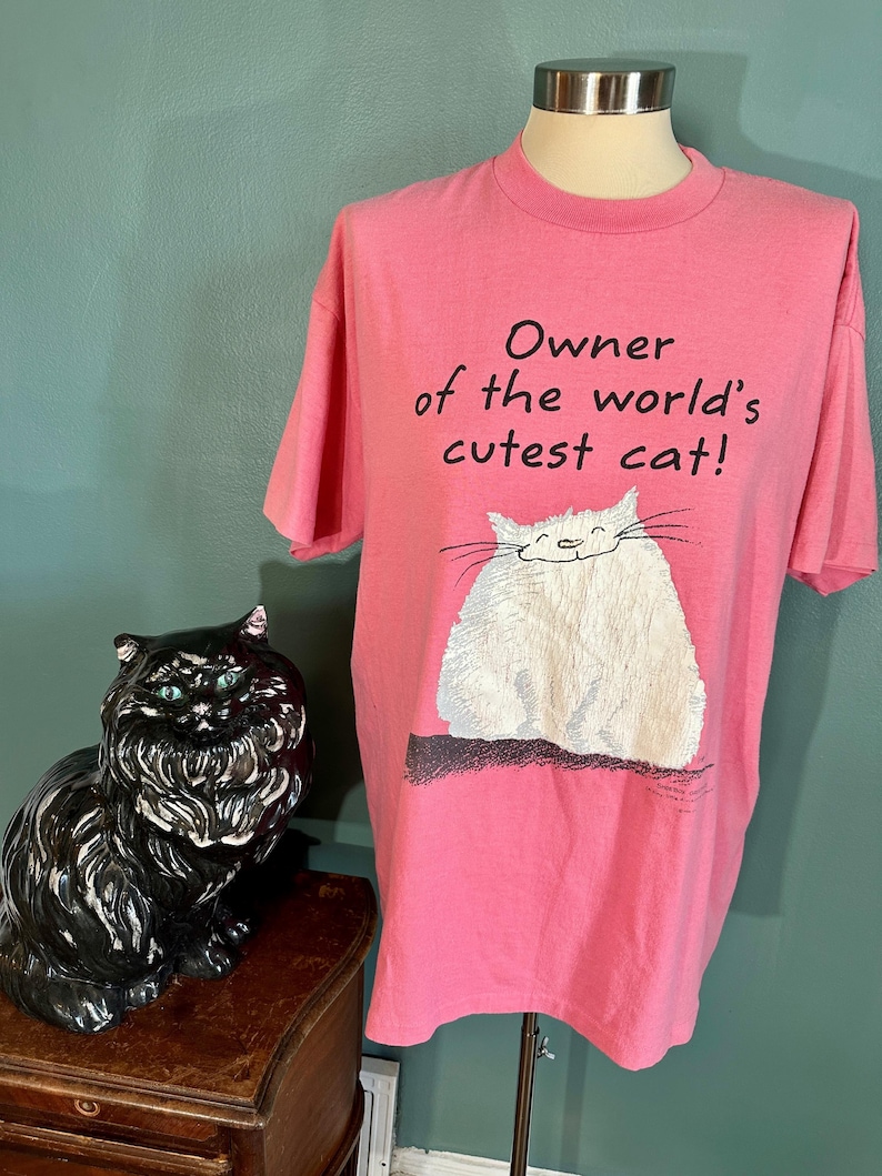 May include: Pink t-shirt with a white cat illustration and the text "Owner of the world's cutest cat!"