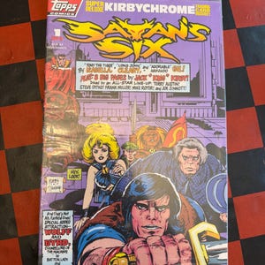 May include: A comic book titled "Satan's Six" with a purple cover, featuring illustrations of various characters. The cover includes text such as "Super Deluxe Kirbychrome" and "Trading Card Inside!" The comic is sealed in plastic.