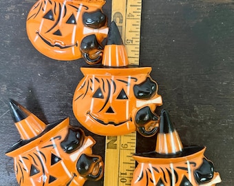 May include: Four orange Halloween pumpkin decorations with black witch hats and cat features. The pumpkins have carved faces with triangular eyes and a smiling mouth. A wooden ruler is next to the pumpkins.