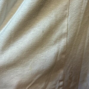 May include: Close-up of a white fabric with a textured surface. The fabric is slightly wrinkled, with a vertical seam running down the center. The material appears to be a soft, possibly knit, textile.