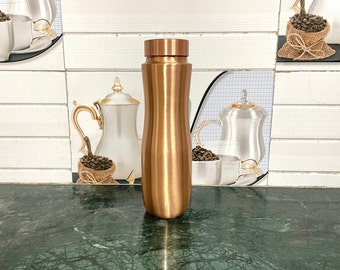 May include: A copper water bottle with a curved shape and a shiny finish. The bottle is sitting on a green marble surface.