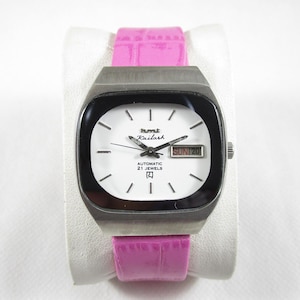Op de afbeelding: Een zilverkleurig polshorloge met een witte wijzerplaat, zwarte wijzers en een zwart datumscherm dat "SUN 20" weergeeft. Het horloge heeft een roze leren band en op de wijzerplaat staat "Humi Kailash Automatic 21 Jewels".