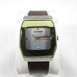 Puede incluir: Un reloj de pulsera cuadrado plateado y dorado con una correa de cuero marrón. La esfera del reloj es blanca con agujas negras y una ventana de fecha que muestra "SUN 20".