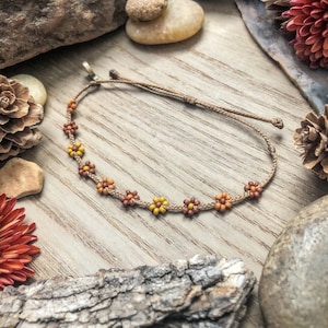May include: A brown cord bracelet with small flower-shaped beads in shades of orange and yellow.