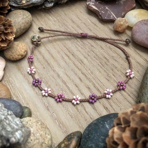 May include: A brown cord bracelet with pink and purple flower-shaped beads.