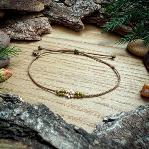 May include: A delicate brown string bracelet with a small pink and green flower charm.