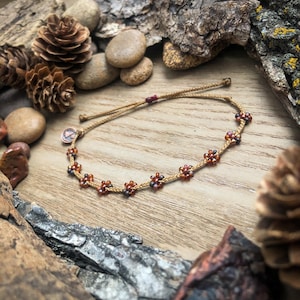May include: A brown cord bracelet with small red and black flower-shaped beads. The bracelet is tied with a knot and has a small metal charm.