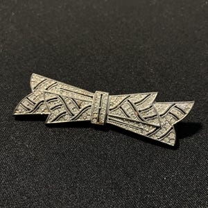 May include: A silver brooch in the shape of a bow, featuring a geometric design and set with clear rhinestones.