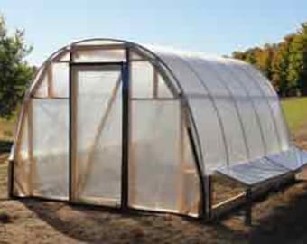 May include: A white plastic greenhouse with a wooden frame and a door. The greenhouse is sitting on a dirt ground.