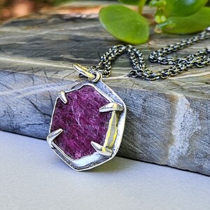 Op de afbeelding: Een zilveren ketting met een hanger met een roze robijn in een geometrische vorm.