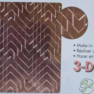 May include: A brown 3-D embossing folder featuring a repeating chevron design. A circular inset displays a close-up of the pattern. The text "Make in: Réaliser un: Hacer en: 3-D" is also visible.
