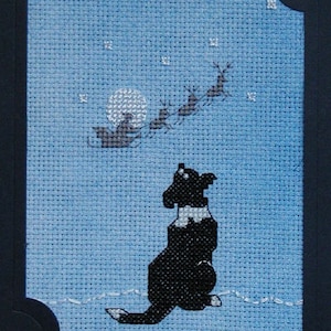 Puede incluir: Un perro blanco y negro sentado sobre un fondo azul, mirando hacia arriba a una silueta de Santa Claus en un trineo tirado por renos que vuelan en el cielo nocturno.
