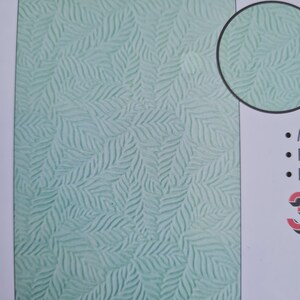May include: A close-up of a textured, light teal surface with a repeating leaf pattern. The leaves have a detailed, veined design. A circular inset shows a magnified view of the leaf pattern. The image is a close-up of a decorative paper or fabric.