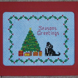 Könnte beinhalten: Eine Kreuzstichkarte mit einem grünen Weihnachtsbaum, roten und gelben Geschenken, einem schwarz-weißen Hund und dem Text "Seasons Greetings".