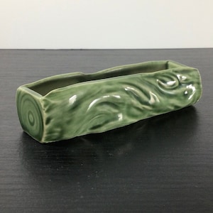 May include: A green ceramic planter shaped like a log with a wood grain design.