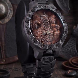 May include: A black wristwatch with a detailed, carved face depicting a Viking figure with birds. The watch has a dark, textured band and a decorative bezel. The watch is displayed on a black stand, with axes and shields in the background.