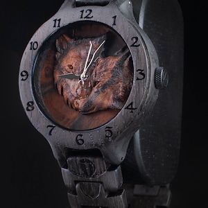 May include: A black wooden wristwatch with a carved wolf design on the face. The watch has a black leather band and a silver face with black numbers.
