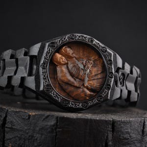 May include: A black wooden wristwatch featuring a carved brown wood dial depicting two figures in an embrace. The watch case and link band are crafted from dark wood with intricate Celtic knotwork patterns engraved around the circular watch face.