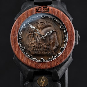 May include: A wristwatch with a black frame and a reddish-brown wooden bezel. The watch face features a relief of a character in armour with the text Fallout and New Vegas. The band is black with a small circular gold-toned emblem featuring a lightning bolt.