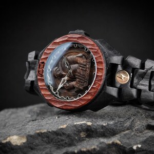May include: A wristwatch featuring a dark black wooden band and a textured reddish-brown wooden bezel. The watch face displays the Fallout New Vegas logo with metallic hands. A small gold-toned circular accent is visible on the watch link.