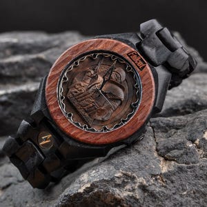 May include: A wooden wristwatch featuring a dark brown circular bezel and a black wooden link band. The watch face displays a Fallout New Vegas graphic with metallic hands and the Fallout logo. A small gold lightning bolt emblem is on the band.