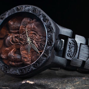May include: A dark wooden wristwatch with a detailed carved face featuring a figure. The watch has a black band with engraved designs and a matching black case. The watch hands are gold-colored.