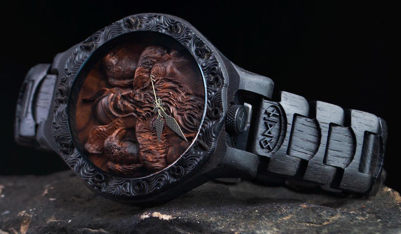 May include: A dark wooden wristwatch with a detailed carved face featuring a figure. The watch has a black band with engraved designs and a matching black case. The watch hands are gold-colored.