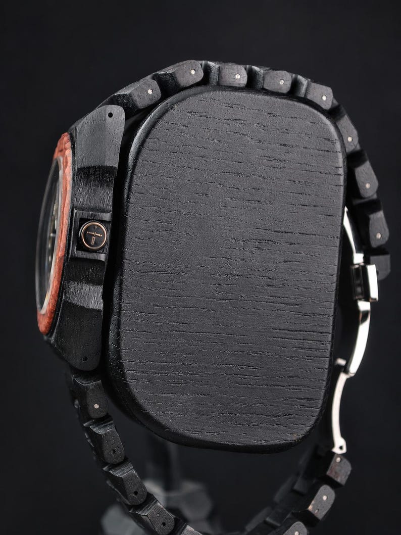 May include: A wristwatch featuring a black wooden case and a matching black wooden link band. The side of the case displays a circular crown with a cross symbol. A reddish-brown wooden bezel surrounds the watch face, and a silver metal clasp is visible.