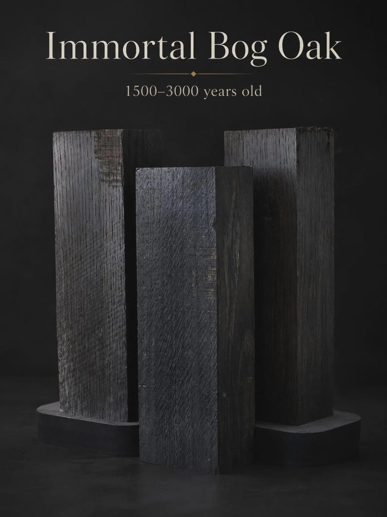 May include: Three rectangular blocks of dark, textured bog oak arranged vertically. The text above reads Immortal Bog Oak 1500-3000 years old. The wood displays a deep charcoal color with visible grain patterns and a weathered, aged surface texture.