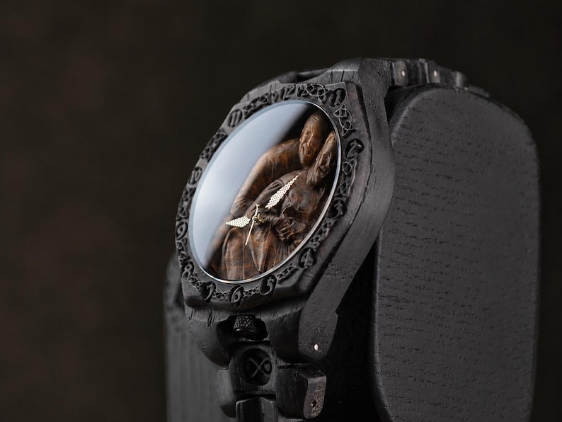 May include: A dark wooden wristwatch featuring a carved relief of two figures on the dial under a glass cover. The bezel has an intricate engraved pattern, and the watch case and band are constructed from dark, textured wood with visible grain.