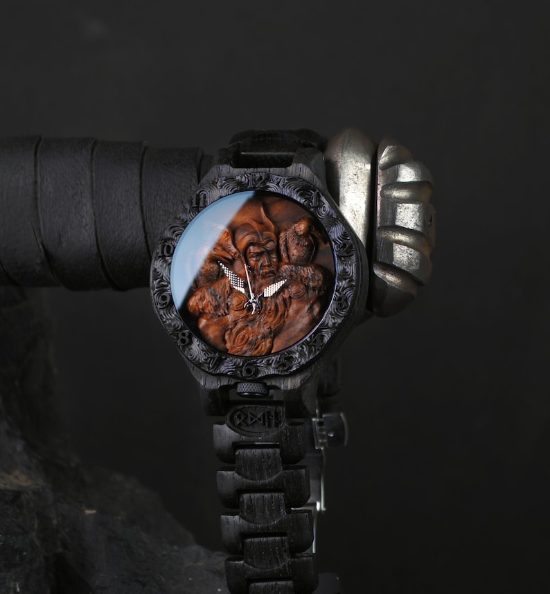 May include: A wooden wristwatch with a detailed carved face featuring a bearded figure. The watch has a dark wood finish, a matching wooden band, and a silver-colored clasp. The watch face is protected by a clear glass cover.