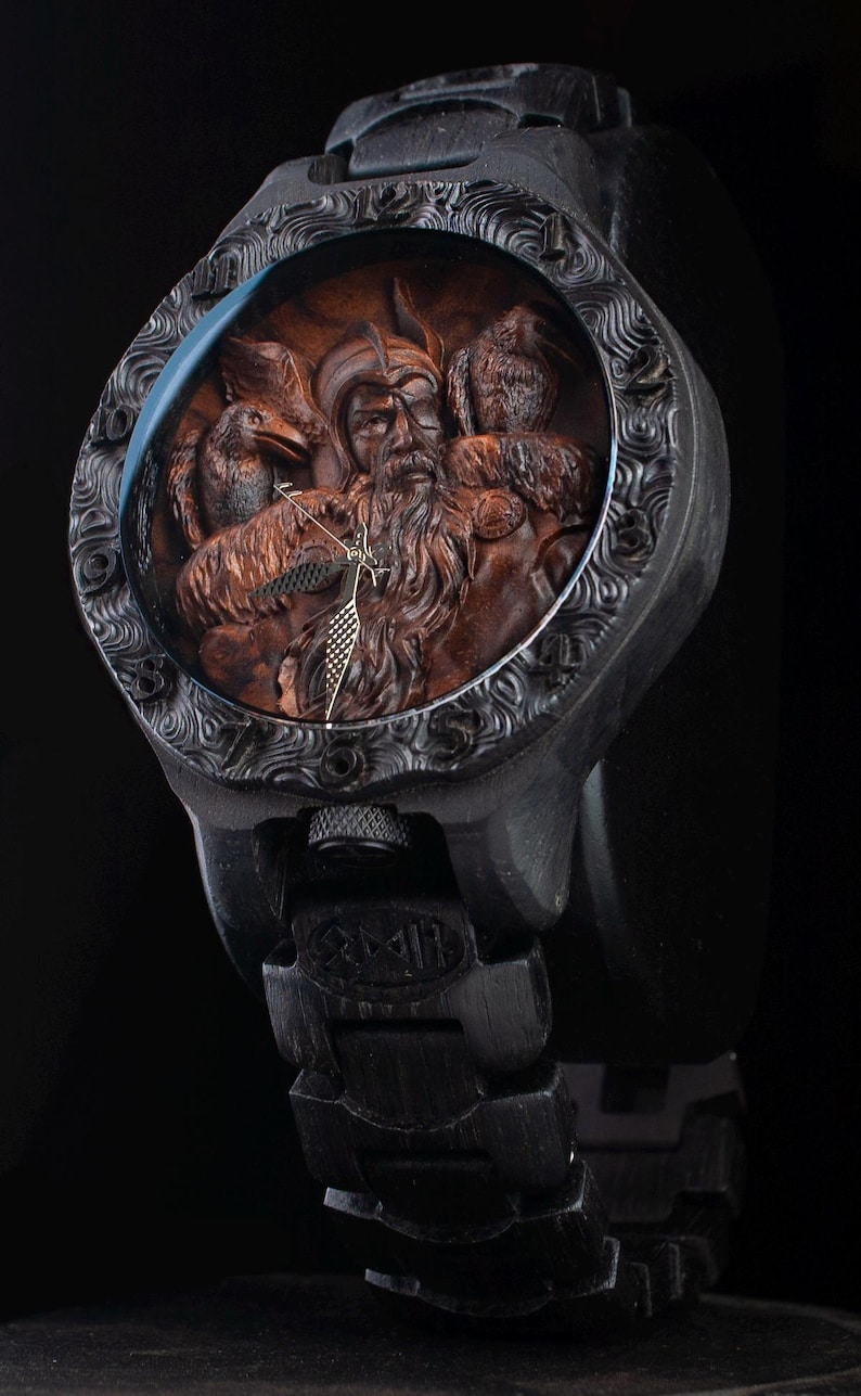 May include: Black wristwatch with a detailed, carved wooden face featuring a bearded figure with birds. The watch has a black band and casing with intricate patterns around the face. The watch face is approximately 1.75 inches in diameter.