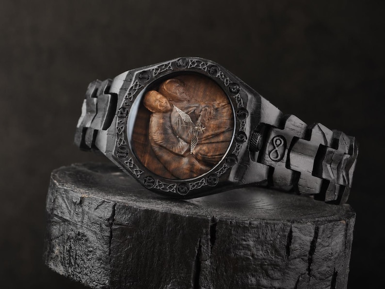 May include: A black wooden wristwatch featuring a dark, textured link band and a circular bezel with intricate Celtic knotwork engravings. The watch face displays a detailed brown wood grain illustration of two figures embracing, with silver hands.
