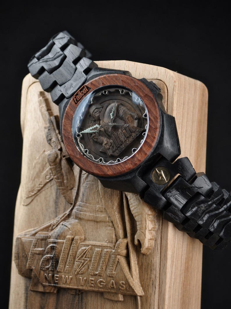 May include: A wooden wristwatch featuring a dark black link band and a reddish-brown circular bezel. The watch face displays the Fallout New Vegas logo and character imagery. It is presented on a carved wooden display stand with the Fallout New Vegas logo.
