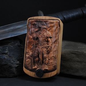 May include: A wooden carving of a warrior in full armor, holding a spear and a flag, set against a detailed landscape. The carving is mounted on a wooden frame. A sword with a leather-wrapped handle is in the background.