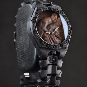 May include: A black wooden wristwatch featuring a carved relief of three figures on the dial. The bezel is engraved with circular symbols, and the link bracelet includes an infinity symbol. Silver-toned hands indicate the time on the dark wood face.