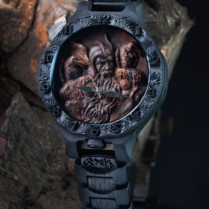 May include: A black wristwatch with a detailed, carved wooden face featuring a bearded figure and two birds. The watch has a black band and a decorative bezel. The watch face is brown and the hands are gold.