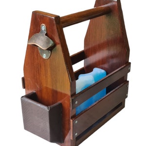 May include: A wooden six-pack beer carrier with a built-in bottle opener and a leather-like pocket. The carrier is stained a dark brown color and has a handle on top. A blue ice pack is inside the carrier.