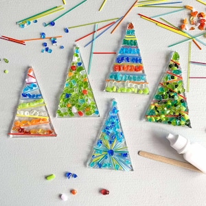 May include: Five handmade glass Christmas tree ornaments. Each tree is a different color scheme, with a clear base and colorful glass pieces. The trees are decorated with red, orange, green, blue, and yellow glass pieces.