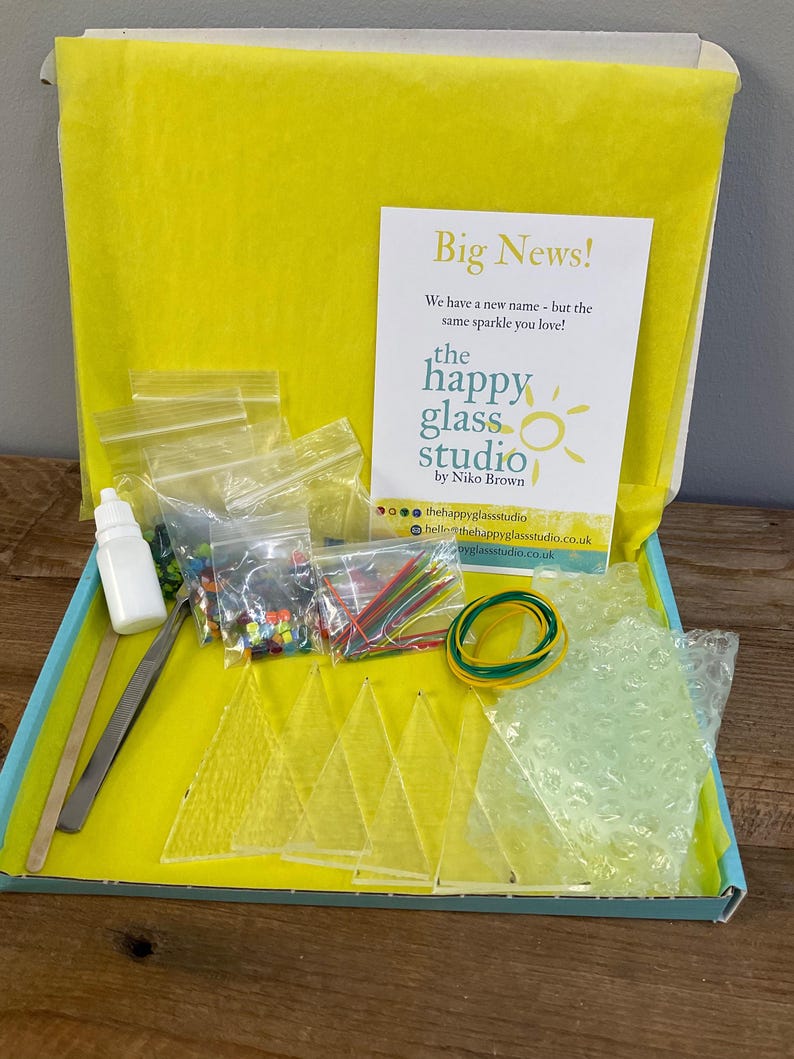 May include: Open box kit from The Happy Glass Studio, containing glass pieces, small bottles, tools, and colorful embellishments. The kit includes a card that reads "Big News!" and "We have a new name - but the same sparkle you love!"