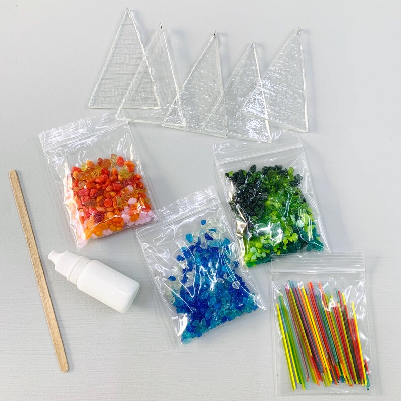May include: A craft kit with clear glass triangle shapes, small bags of colorful beads, a white bottle, and a wooden stick. The beads are in shades of red, orange, green, and blue, and there are also small colorful sticks.