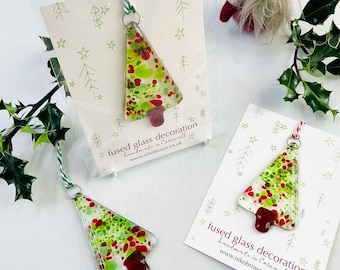 Könnte beinhalten: Weihnachtsbaumschmuck aus geschmolzenem Glas mit grünen, roten und weißen Akzenten. Jeder Baum hat eine rote Basis und ist an einer Karte mit dem Text "fused glass decoration handmade in Cornwall" befestigt.