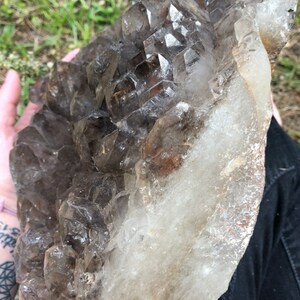 May include: A large, clear quartz crystal cluster with smoky quartz crystals. The cluster is raw and has a natural, rough texture.