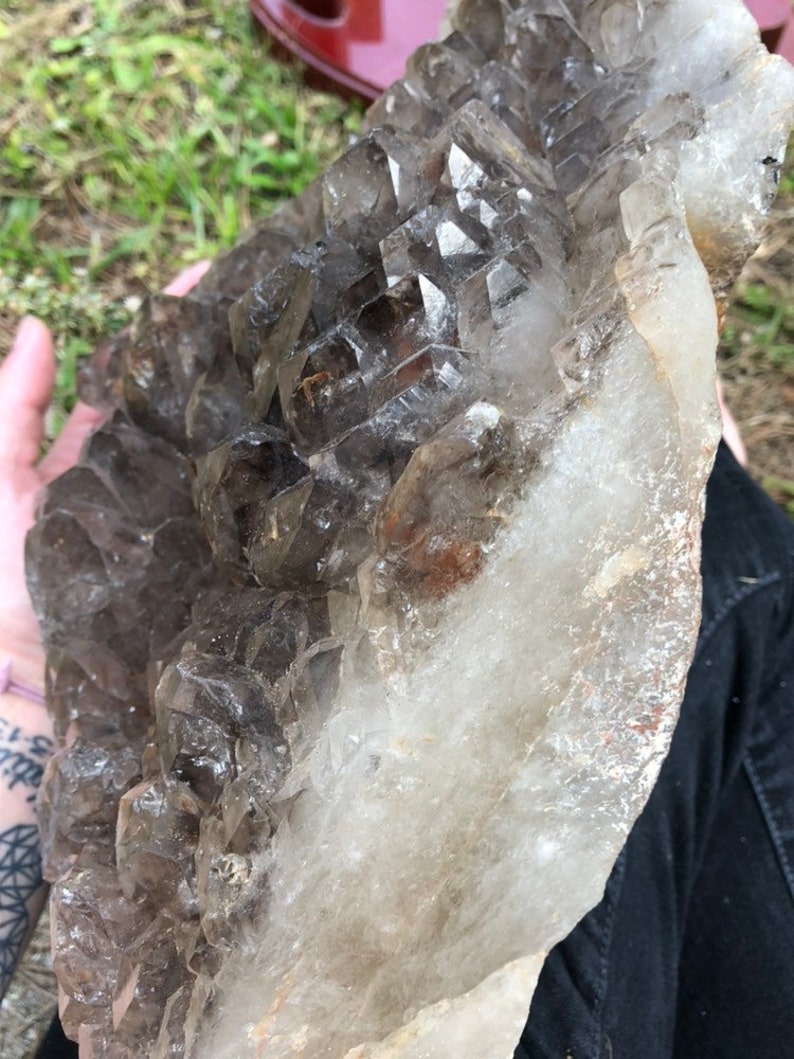 May include: A large, clear quartz crystal cluster with smoky quartz crystals. The cluster is raw and has a natural, rough texture.