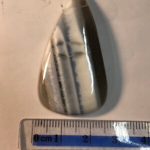May include: A teardrop-shaped cabochon of white and gray banded agate, measuring approximately 3 cm in length. The stone has a smooth, polished surface and is suitable for jewelry making.