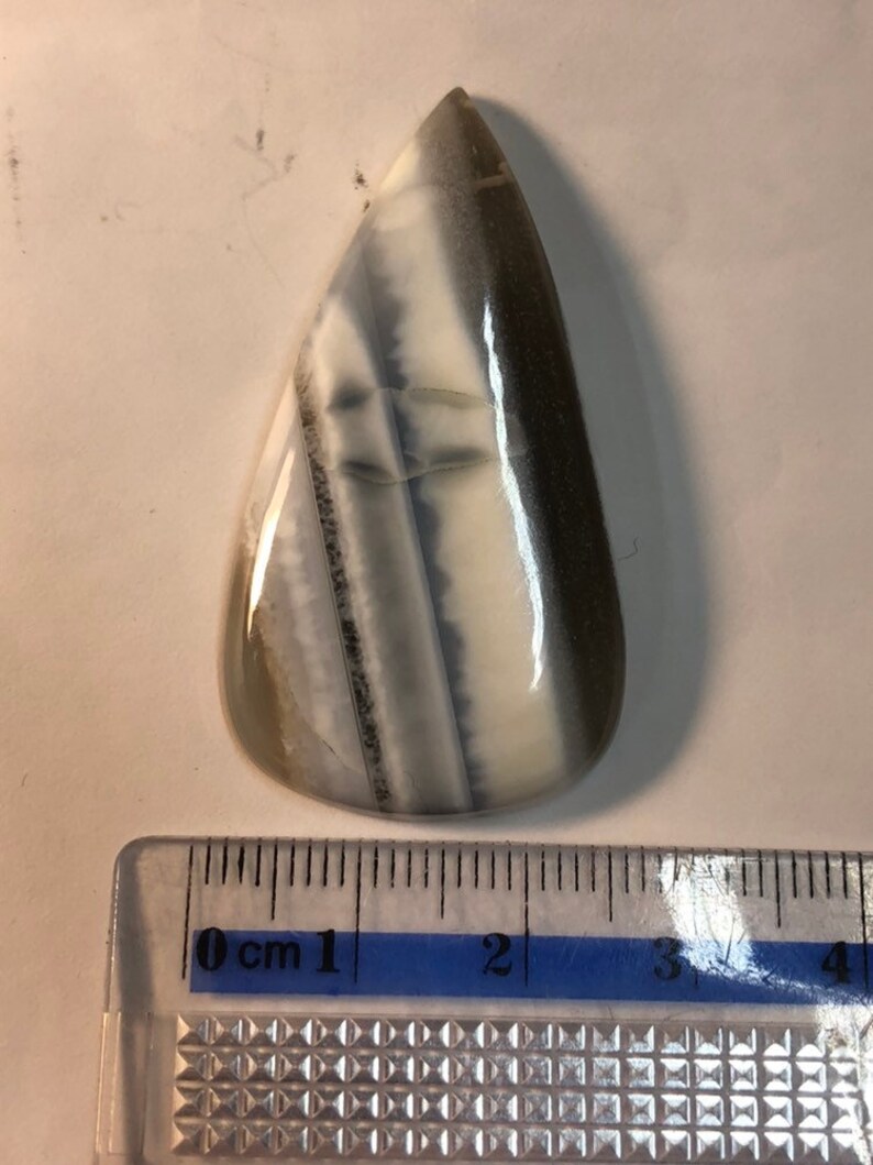 May include: A teardrop-shaped cabochon of white and gray banded agate, measuring approximately 3 cm in length. The stone has a smooth, polished surface and is suitable for jewelry making.